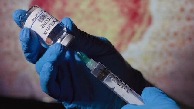 doctor filling a syringe with monkeypox vaccine in front of a monitor with the monkeypox virus displayed