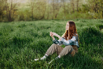 Fototapeta premium A young beautiful woman sits on the green grass in the park and looks out into the setting sun