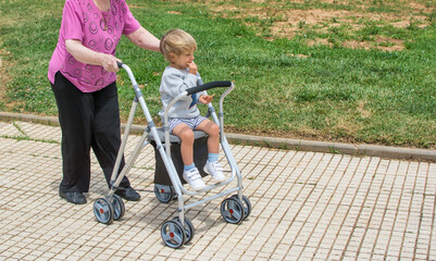 Grandmother with walker playing with her great grandson. Old lady with walker walking in the park.

