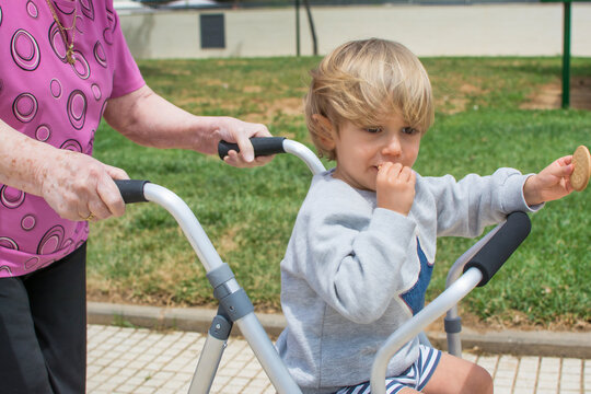 Grandmother with walker playing with her great grandson. Old lady with walker walking in the park.