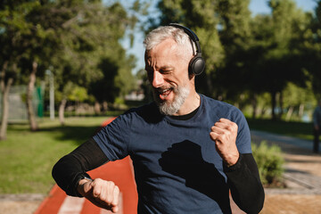 Happy mature male handsome runner listening to the music in headphones checking physical activity...