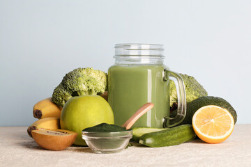 green smoothie in glass bottle, spirulina powder, vegetables and fruits on blue background. healthy, raw, vegan diet concept. copy space