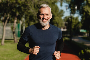 Cropped closeup portrait of a male mature athlete sportsman runner jogging in the morning in public...