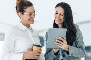 Two attractive young business women working with digital tablet while talking and walking in a modern startup.