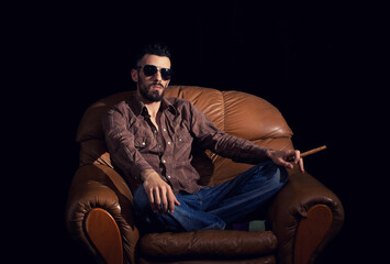 Man with glasses sitting with habano in brown leather armchair