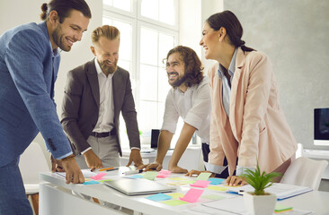 Brainstorming. Cheerful creative colleagues write notes on colorful stickers while developing business project in office. Concept of teamwork, brainstorming and creative thinking.