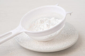 Icing sugar in a plastic sieve on top of white ceramic plate.