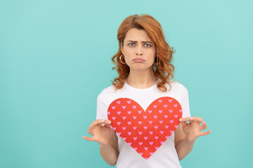 confused redhead girl hold red heart on blue background