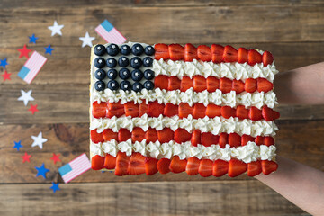 Hand serving cake with US flag colors on wooden background with decoration. Independence Day...