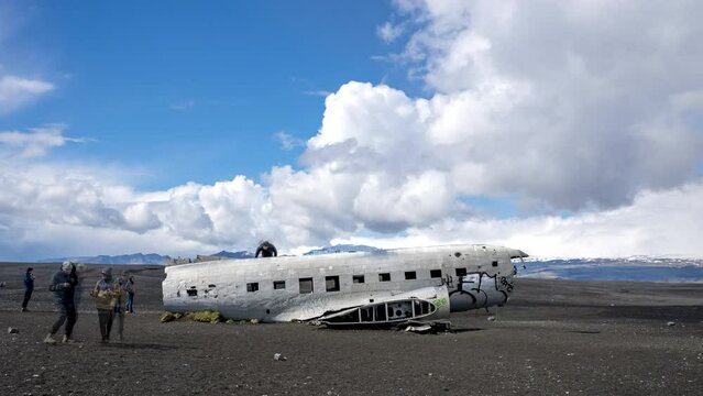 4k timelapse of plane wreck on black sand beach in Iceland. Cloudy blue sky with tourists walking around the plane.