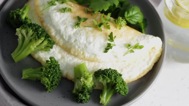 Protein omelet with broccoli and greens on a gray plate with lemonade.Healthy food concept. Rotate video