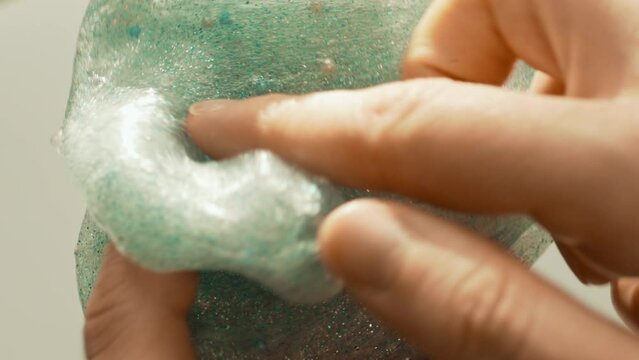 Playing with textured slime with sparkle shining glitter, stretching the gooey substance toy for fun and stress relief.