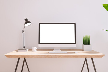 Blank white modern computer monitor on wooden table with coffee mug, lamp and green plant in small pot on light wall background. 3D rendering, mock up