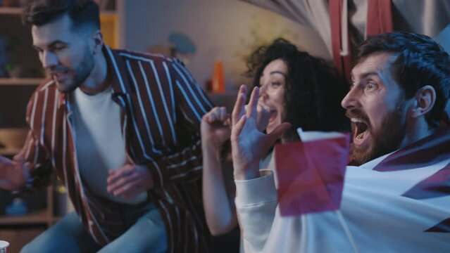 Diverse multiracial friends watching football match on tv at home with enthusiasm, cheering corner kick and rejoicing for a goal. People embracing with each other at home.