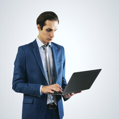 Young businessman in blue suit working with modern laptop, isolated on light grey wall background, close up