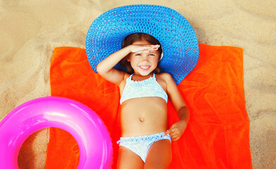 Summer portrait child little girl with inflatable ring wearing straw hat lying on the sand on beach