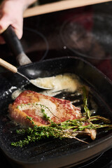 Close-up of unrecognizable chef cooking beef steak with butter and rosemary, thyme sticks on hot grill pan