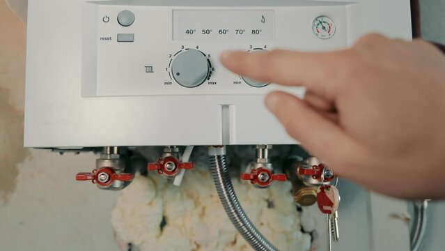 Switching on the home boiler. The beginning of the heating season. The man's hand turns on the boiler and sets the temperature of heating and hot water.