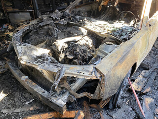 Fototapeta na wymiar Car that is entirely burned up by fire. The aftermath of a garage fire with the car in ruin. Metal scorched and ash everywhere