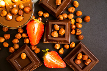 Dark chocolate, fresh strawberries, nuts on a dark background