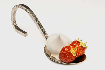 Strawberries with cream lie on a large chrome spoon. White background.