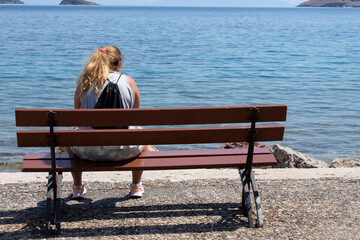 woman  sitting on a bench by the sea. sunny summer day with blue sky