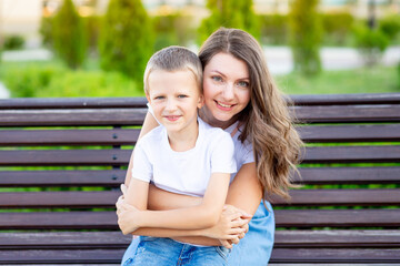 mom and her baby son in the park on a bench in the summer have fun hugging, laughing and playing