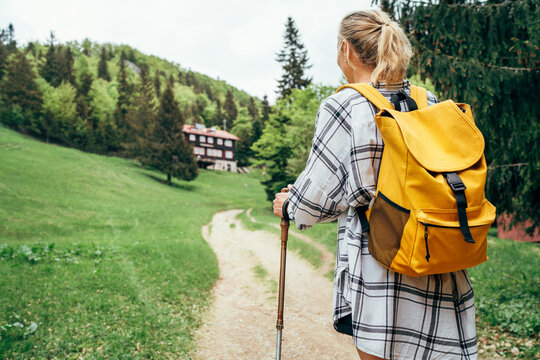 Lonely female with yellow backpack walking by mountain path with trekking poles to mount refuge hut in Slovakia, Mala Fatra region. Active people and European mountain hiking tourism concept image.