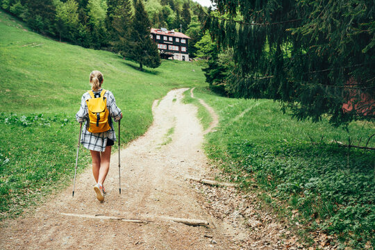 Lonely female with yellow backpack walking by mountain path with trekking poles to mount refuge hut in Slovakia, Mala Fatra region. Active people and European mountain hiking tourism concept image.