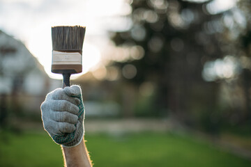 Close-up, a man's hand in a work glove with a paintbrush against the background of a rural landscape