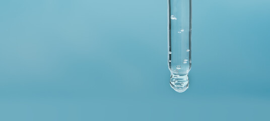Closeup of pipette with serum, hyaluronic acid on blue background. Cosmetics and healthcare concept. Dose of essential oill, retinol with air bubbles. Beauty product presentation, front view, macro