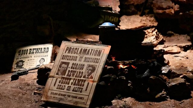 Jesse James wanted poster leans up against campfire and coffee pot in cave hideout near Ozark USA. Gang of robbers and folk heroes often hit loot in caverns until law stopped looking for them.