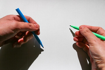 two skillful hands of an ambidextrous young man drawing with blue and green ink markers colors on a...