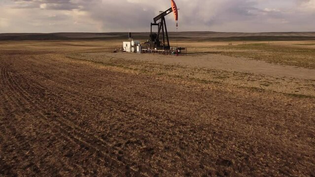 Aerial Tilt Reveal Of An Oil And Gas Industry Pump Jack On The Alberta Prairies With A Seeded Field And Storm Sky.
