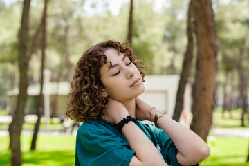 Naklejka premium Side view of young redhead woman wearing green tshirt standing on city park, outdoors relaxing with eyes closed, feeling alive, breathing, dreaming.
