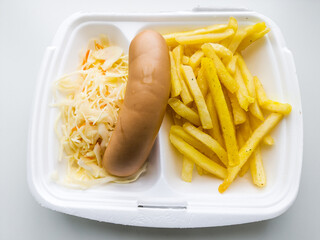 Food in disposable lunch box. French fries, sausage, cabbage and carrot salad.