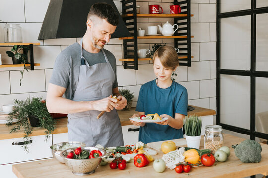 Family Dad Young Man And Son Teenage Boy Cook Vegetable Salad In Kitchen And Spend Quality Time Together, Father And Son Talking And Cooking Vegetarian Food And Doing Chores, 8 March And Mothers Day