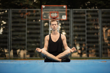 Mental and physical health. Yoga and healthy lifestyle concept. Young sporty man practicing yoga in the city. Handsome muscular man sitting in lotus position.