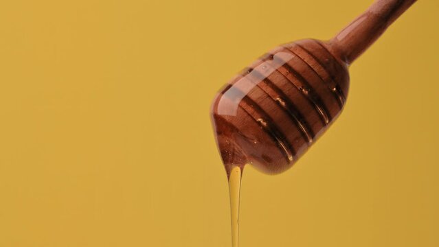 Healthy Food Concept. Delicious sweet liquid honey flows down from a wooden spoon on yellow background. Organic healthy honey, vitamins, sweet dessert. Honey dripping from a spoon
