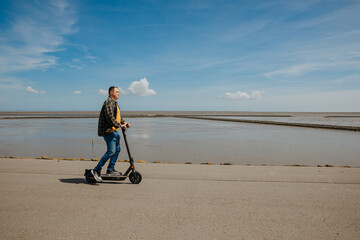 You ride an electric scooter along the beach. Electromobility in Germany. North Sea at low tide
