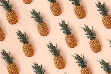 A bright pattern of many pineapples on a trendy soft beige pink background. Tropical ripe juicy fruit flat lay for your design projects. Summer concept