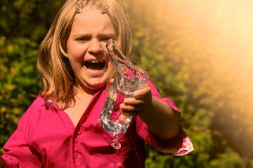 Fototapeta premium The child splashes water from a glass in a rage . A young girl screams and swears. Child aggression .