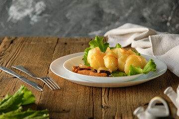whole boiled potatoes with bacon and onions, cracklings and fried onions, rustic lunch, on a wooden...