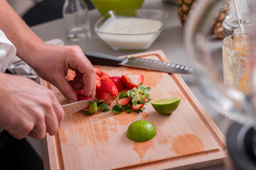 Man cutting strawberries and limes on chopping board.