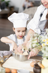 Mother and daughter baking homemade sweet pie together, having fun. Home bakery, family time, little kids in process of food preparation in the kitchen at home, helping mother, doing chores