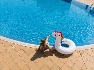 Beautiful woman with unicorn pool float in pool in the hotel. Summer holidays. Aerial top view from drone