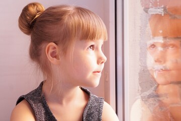 Beautiful little girl with high hairstyle looks out windows.