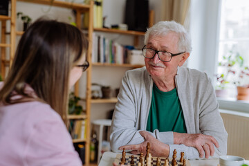 Adult daughter visiting her senior father at home and playing chess together.