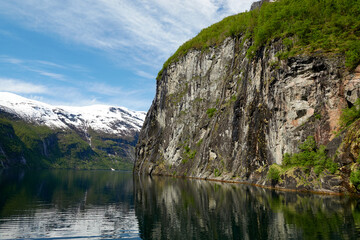 Fototapeta na wymiar Geirangerfjord. Spring in the norwegian fjords. Reflections. Fishing. Waterfalls. Trees. Boats. Light and clouds. 