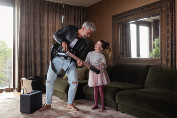 Father rock guitarist having fun and dancing with his little daughter at home.
